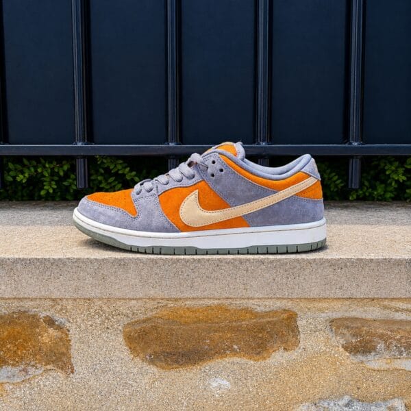 Nike SB Dunk Low orange et grise en suede photographiée de profil sur un muret en pierre