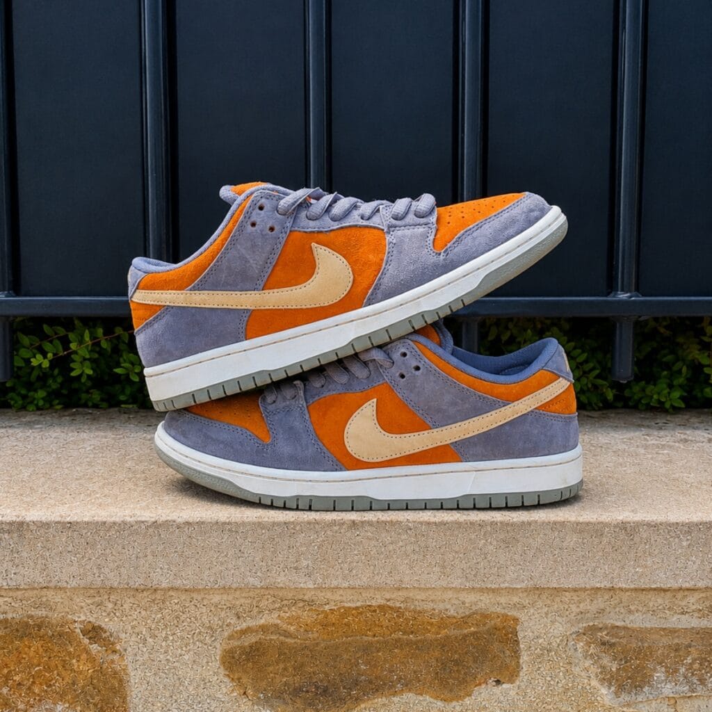 Paire de Nike SB Dunk Low orange et grise empilée sur un muret extérieur en pierre